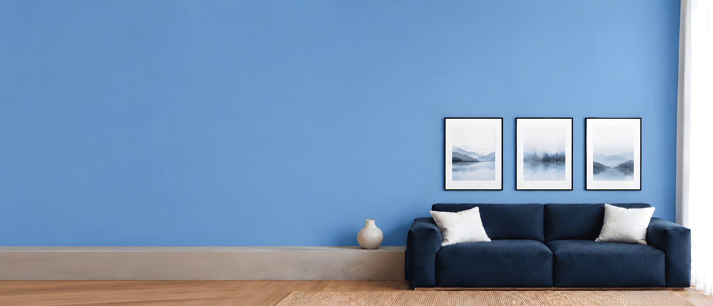 Three framed prints in a row above a navy sofa on a blue wall
